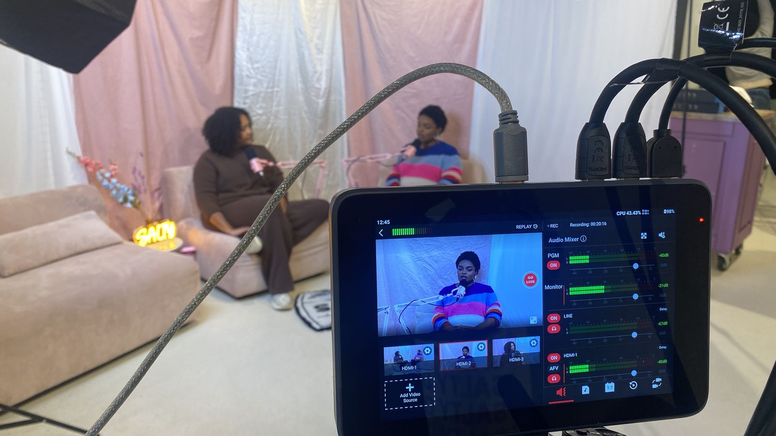 Livemixer met camerabeelden en audioniveaus voor twee gasten op een roze set