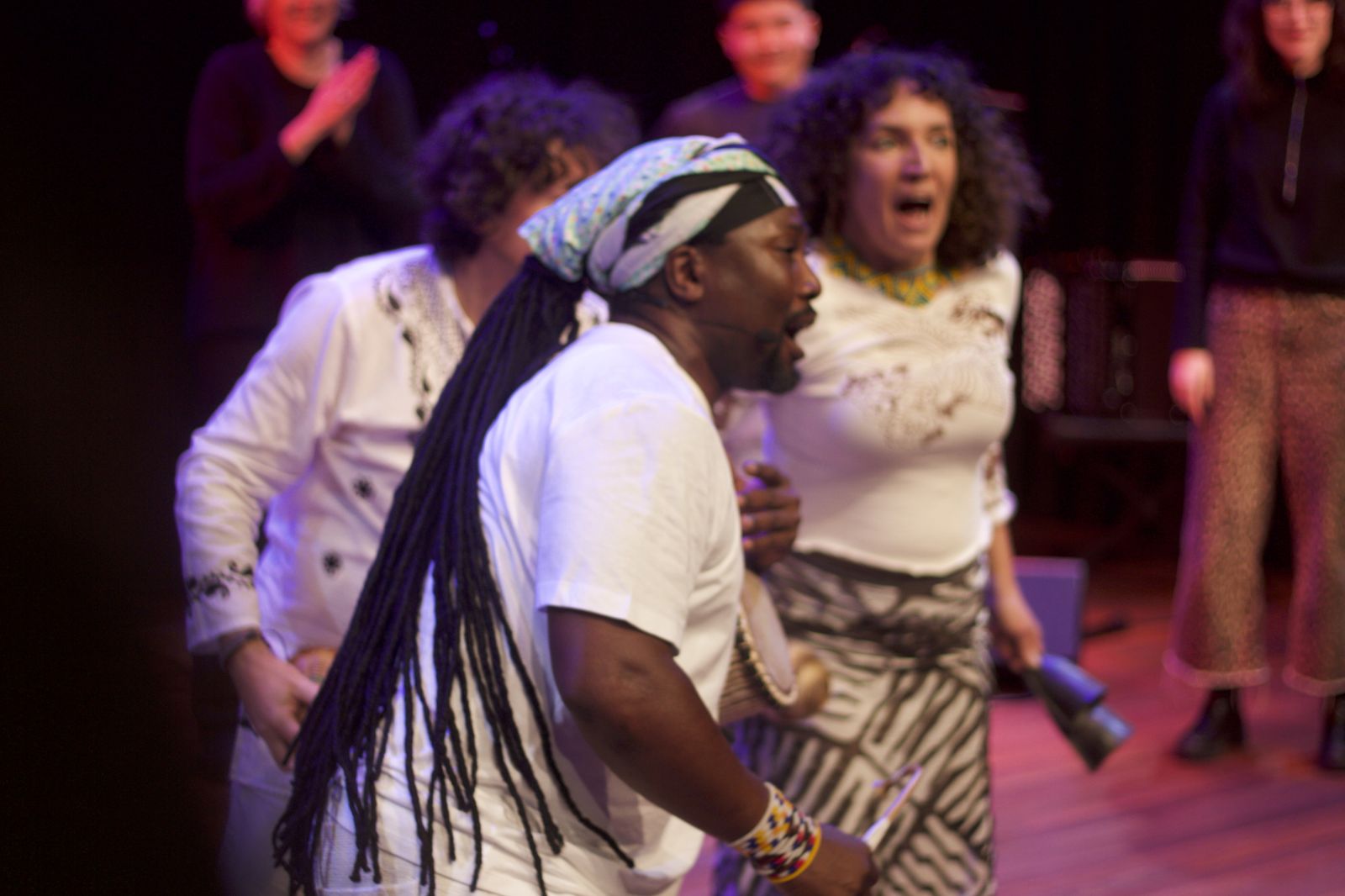 Muzikant met lange dreadlocks en hoofddoek zingt op het podium, publiek klapt mee